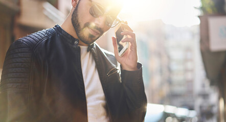 Crop young bearded man using smartphone outside modern building