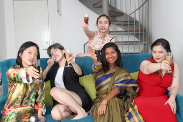 Young southeast asian woman group talk celebrate sing making funny mocking faces expression drinking cheering cheers on blue living room sofa