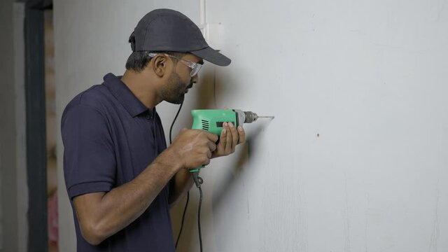 Electrician drilling wall using drilling machine - concept of home renovation, skilled profession and serviceman