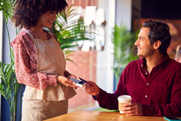 Man Paying Female Server In Coffee Shop Using Debit Or Credit Card