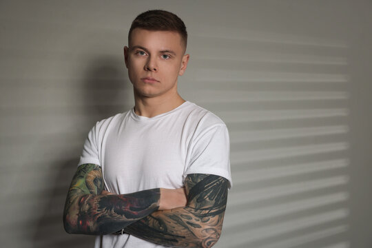 Young man with tattoos near light wall. Space for text