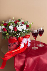 Floral arrangement in hat box and wine in glasses on beige background. Space for text. Concept of date