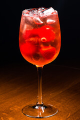 aperol cocktail with strawberries in transparent high glass on dark background