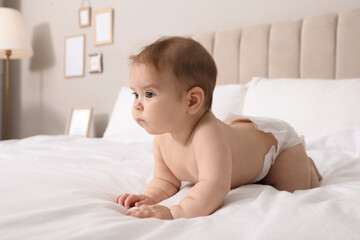 Cute little baby in diaper on bed at home