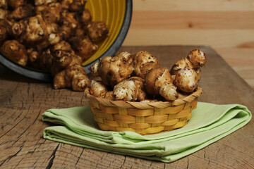 Fresh Jerusalem artichoke tubers are stored in a basket on a wooden table