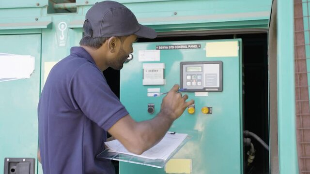 Electrical engineer noting down voltage flow of switch gear or current distribution board at industrial company - concept of blue collar job, professional occupation and maintenance service.