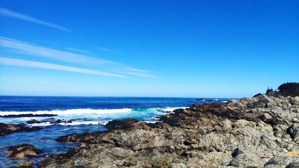 Waves crashing on a rocky beach and blue sky background at Isla Negra, Chile.