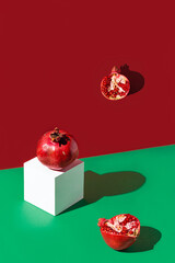 Creative composition made of fresh pomegranates on green and red background with white cube and shadows. Minimal style. Refreshment concept. Healthy food ingredient theme.