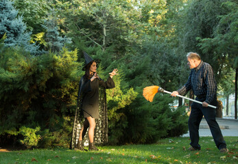 A young beautiful girl in a witch's costume is trying to bewitch a man who is holding a garden...