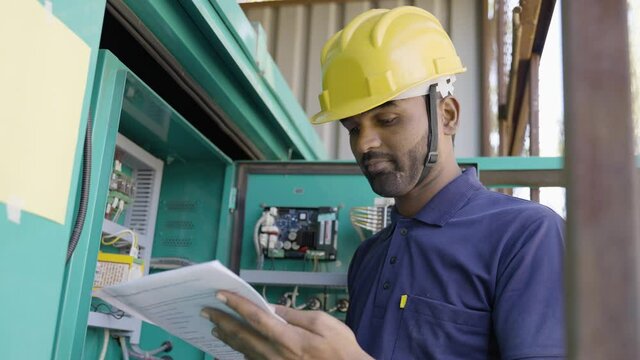 young indian electrician reading or inspecting voltage flow of switch gear or current distribution board at industrial company - concept skilled profession and maintenance service.