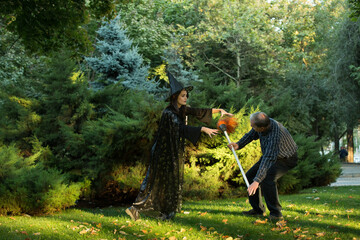 A young beautiful girl in a witch's costume is trying to bewitch a man who is holding a garden...
