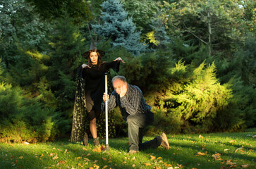 A young beautiful girl in a witch's costume is trying to bewitch a man who is holding a garden...