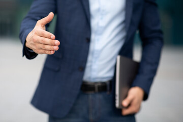 Unrecognizable businessman with laptop giving hand, greeting business partner