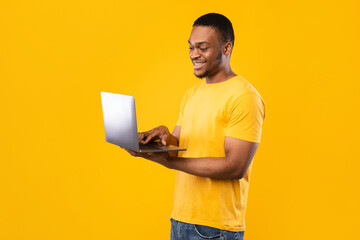Happy African American Freelancer Man Using Laptop Over Yellow Background