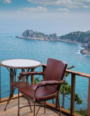 Tables and chairs on the balcony of an unoccupied hotel. Overlooking the sea and with a mountain background.