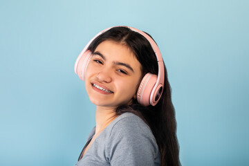 Indian teen girl in casual wear listening to music in pink wireless headphones, enjoying cool song on blue background