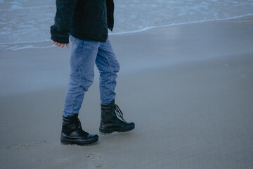 in black massive boots walks along the sandy beach, the lower part of the male body