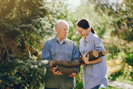 Grandfather with granddaughter on a yard with firewood in hands