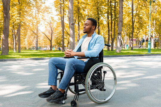 Full length of peaceful black handicapped guy in wheelchair having walk at urban park in autumn