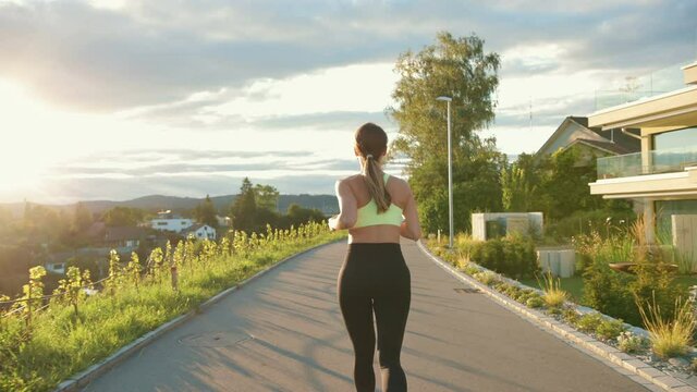 Back view of the caucasian young woman athlete running on street outside the city alone. Pretty happy sportswoman jogging doing cardio workout. Sporty lifestyle, outdoor workout, athletic concept