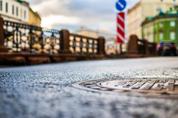 Rainy day in the city. The empty road. Rainy day in the city. The road after the rain. Focus on the manhole cover. Close up view of a manhole cover at the level of the asphalt.