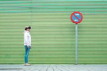 Photo with copy space of a man standing with virtual reality goggles next to a green wall outdoors