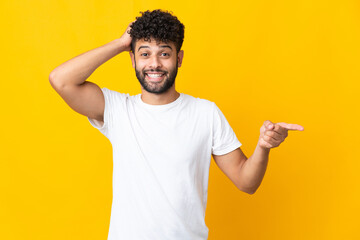 Young Moroccan man isolated on yellow background surprised and pointing finger to the side