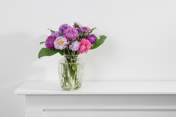bouquet of colorful asters are on a white dresser. Copy space