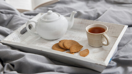 Fototapeta na wymiar interior and home coziness concept. Top view. A cup of tea, a teapot with herbal tea, sugar bowl on a wooden tray on the bed. Porcelain cup