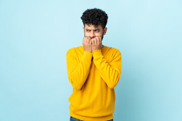 Young Moroccan man isolated on blue background nervous and scared putting hands to mouth