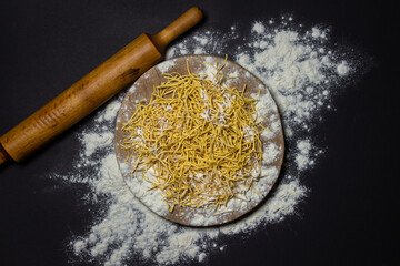 Egg noodles in flour on a black background. Dry homemade noodles on a wooden board. Traditional pasta