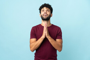 Young Moroccan man isolated on blue background keeps palm together. Person asks for something