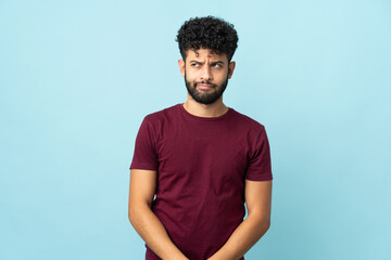 Young Moroccan man isolated on blue background having doubts while looking up