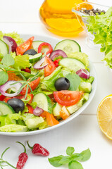 Healthy fresh vegetable salad with tomatoes, cucumbers and bell peppers in a plate on a white wooden background