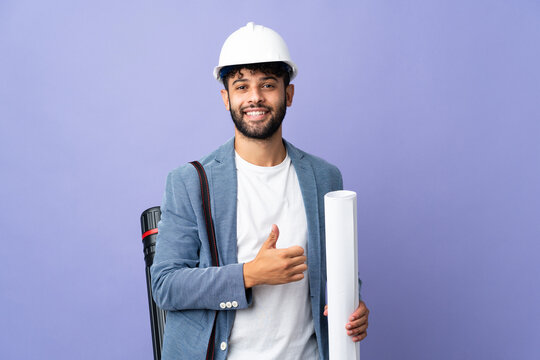 Young architect Moroccan man with helmet and holding blueprints over isolated background giving a thumbs up gesture