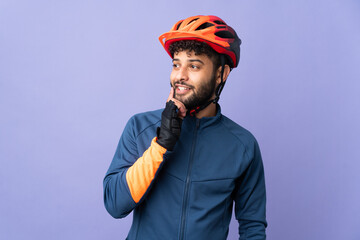 Young Moroccan cyclist man isolated on purple background thinking an idea while looking up