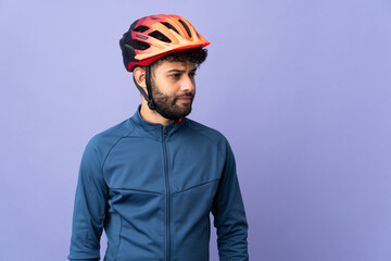 Young Moroccan cyclist man isolated on purple background looking to the side - obrazy, fototapety, plakaty