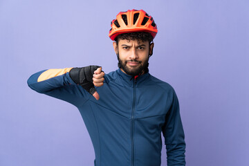 Young Moroccan cyclist man isolated on purple background showing thumb down with negative expression