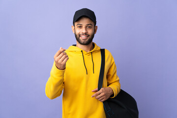 Young sport Moroccan man with sport bag isolated on purple background making money gesture