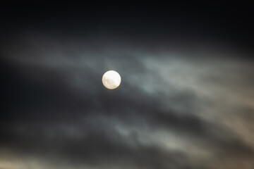 The sun is big behind the clouds.