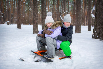 Fototapeta na wymiar In winter, two happy girls girlfriends sit on a snow scooter in a snowy forest.