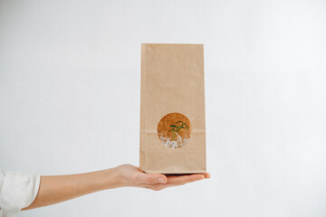 Hand holding a paper bag with a green plant showing through a window in it.