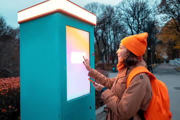 A woman uses a self-service kiosk to print photos from her smartphone on a city street