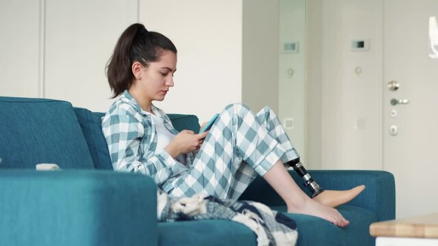 Serious woman with artificial bionic high technology leg prosthesis texting by phone at home