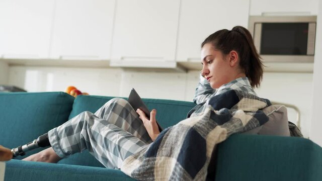 Positive woman with artificial bionic high technology leg prosthesis texting by tablet at home