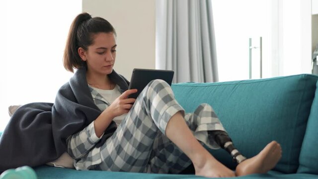 Handsome woman with artificial bionic high technology leg prosthesis texting by tablet at home