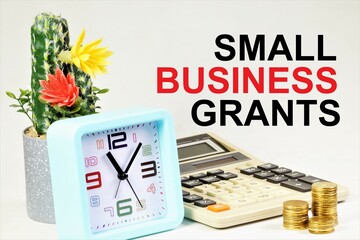 Small business grants. The inscription of the motivation concept on the background of a calculator, cash coins and hours of planning.