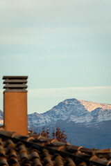 Vertical view of the snowy Mulhacen (Sierra Nevada, Spain) behind a tiled roof with a chimney