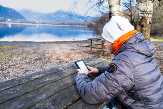 Young man reading an e-book on digital tablet device in outdoor at winter on a mountain lake