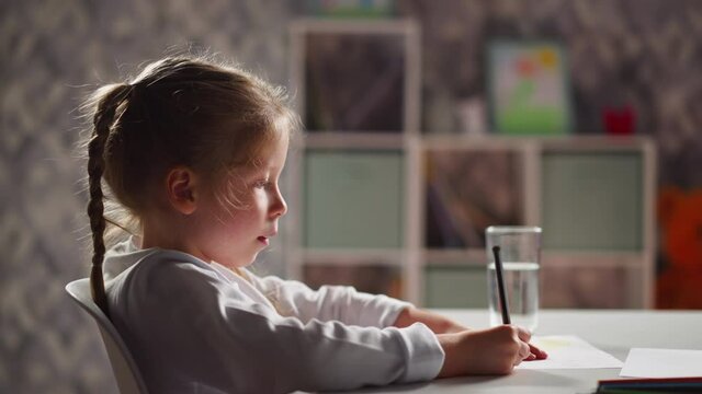 Unhappy girl draws picture sitting at table in kindergarten